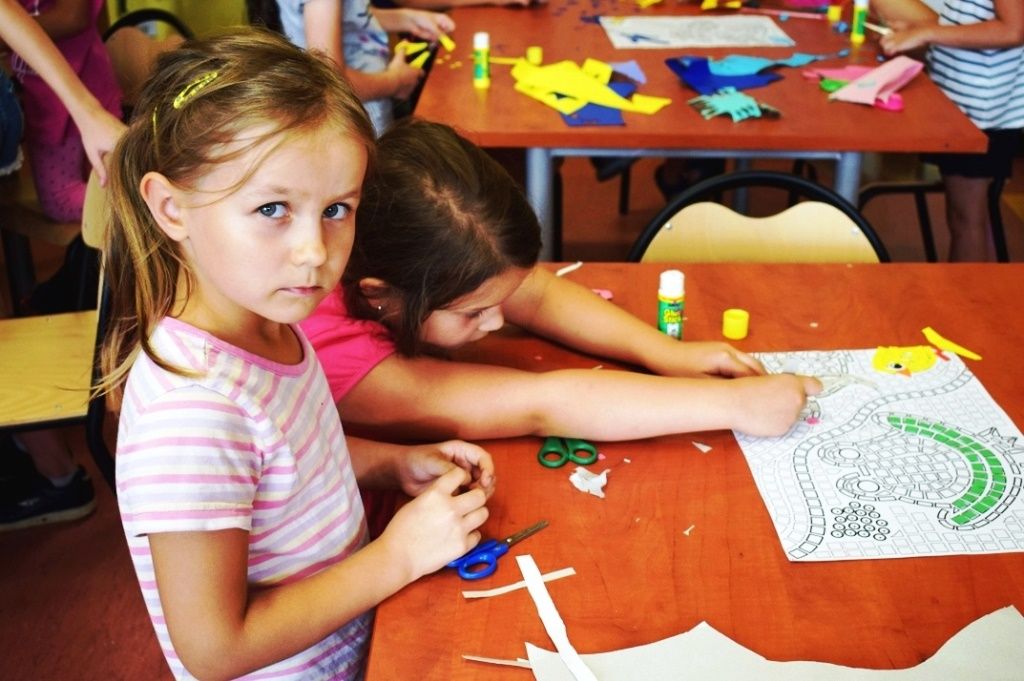 dwie dziewczynki przy stole wykonują mozaikę z papierowych elementów